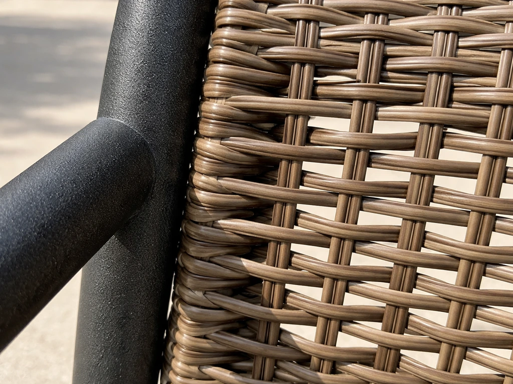 Closeup of anti-rust powder-coated steel frame beside hollow synthetic wicker weave outdoors.