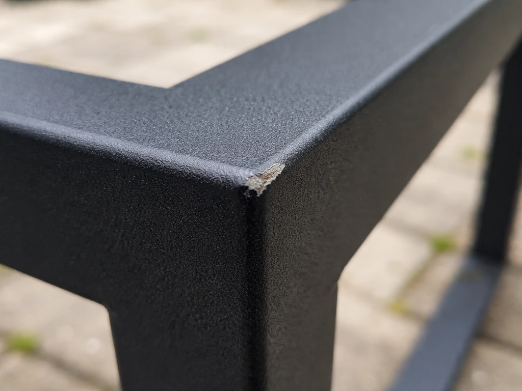 Macro close-up of powder-coated steel frame with a chipped edge revealing layered coating.